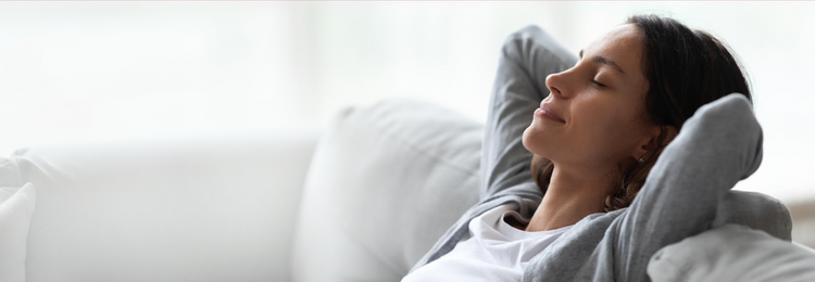 Relaxed woman resting on a sofa with eyes closed – calming herbs for relaxation.