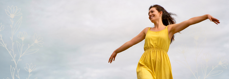 Joyful woman in a yellow dress with arms outstretched outdoors – herbal supplements for immune health.